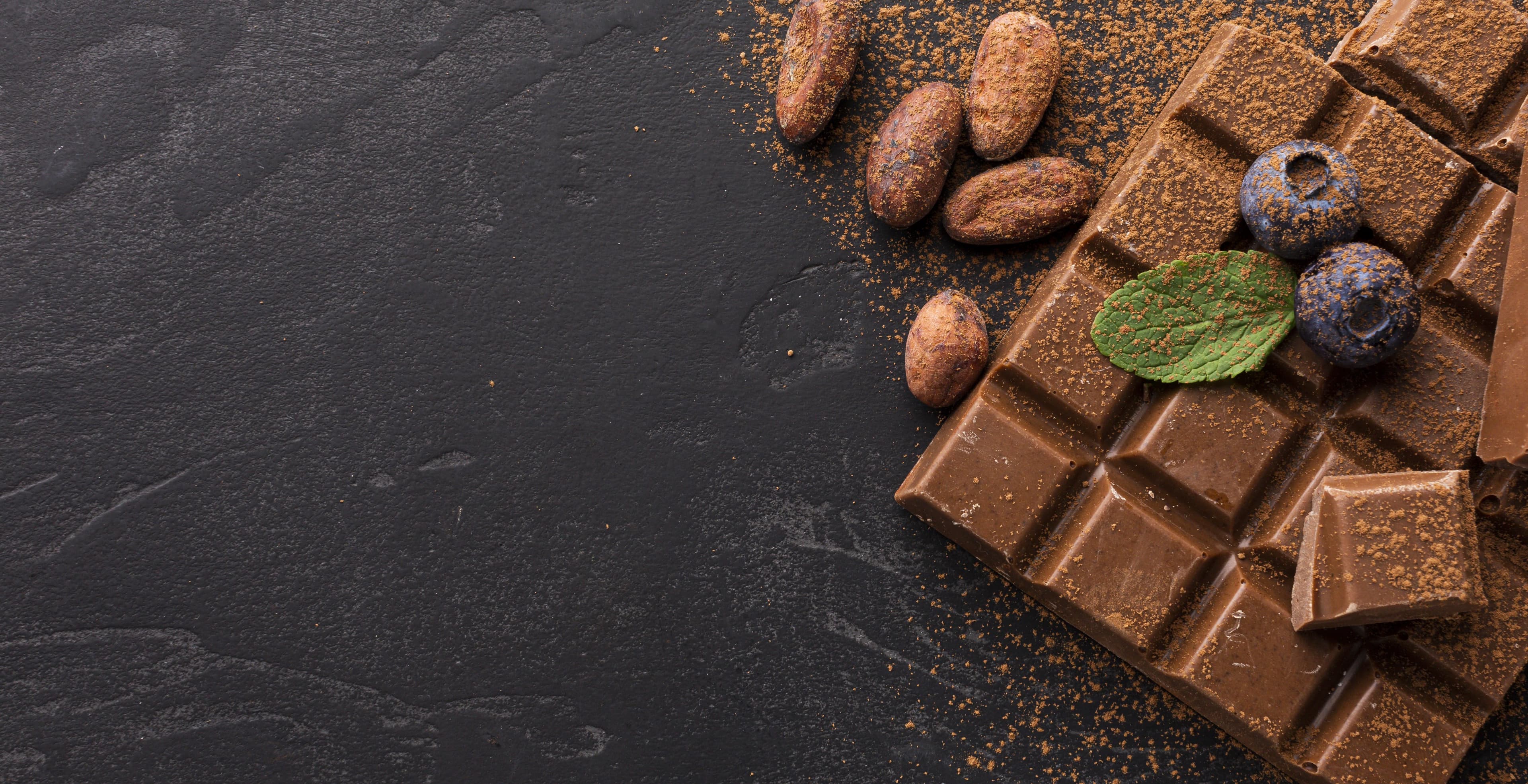 A tempered bar broken over slate, scattered with roasted cacao beans